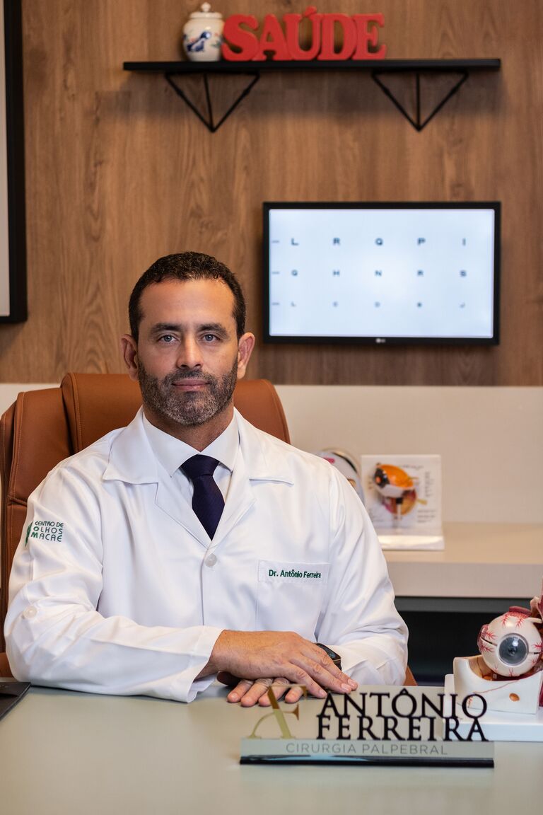 Dr. Antônio Ferreira Leite Jr. em sua mesa no consultório, com um modelo anatômico do olho
