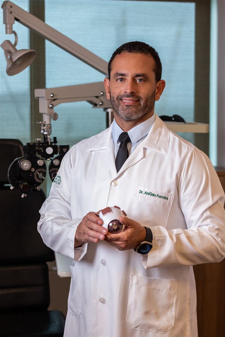 Dr. Antônio Ferreira em consultório oftalmológico, segurando um modelo anatômico do olho
