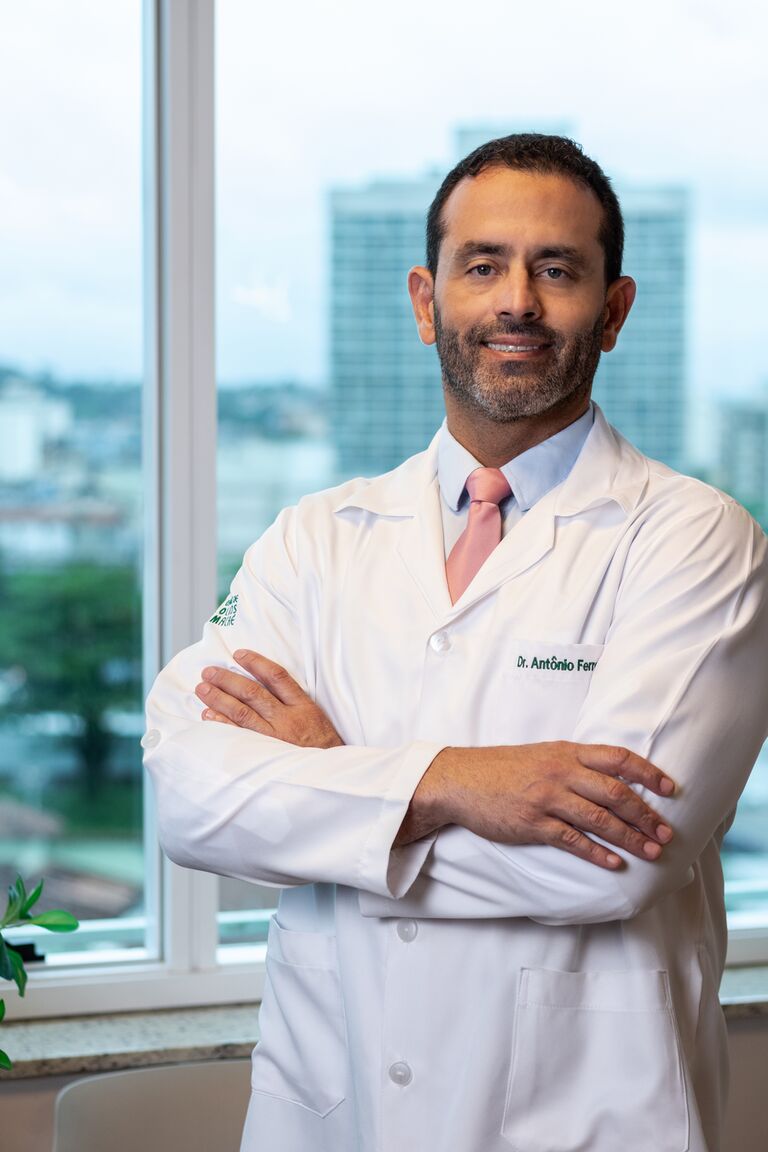Dr. Antônio Ferreira Leite Jr. de braços cruzados, junto a uma janela iluminada